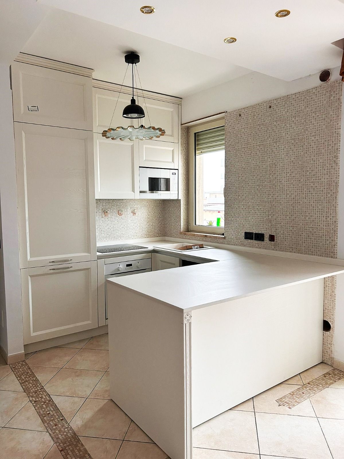 Una piccola cucina con mobili color crema, un'isola, un forno a microonde e una finestra con le persiane.