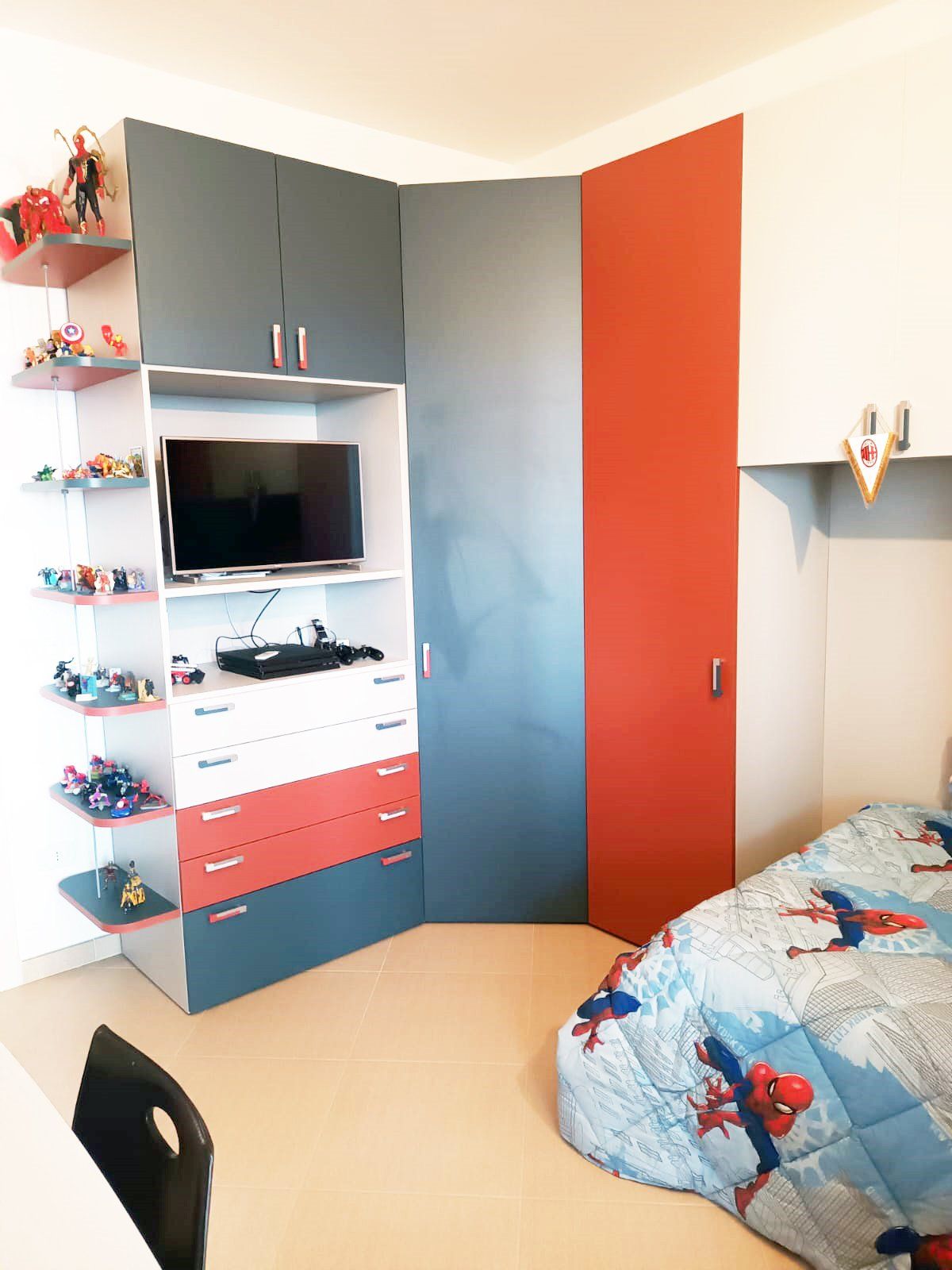 Cameretta per bambini con armadio/scaffale angolare. Mobile rosso, grigio e bianco con TV e giocattoli. Biancheria da letto di Spider-Man.