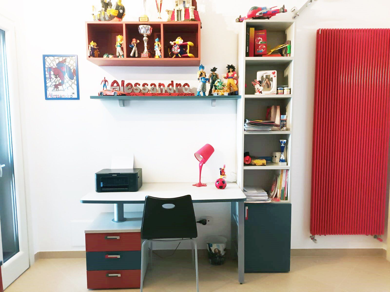 Scrivania per bambini con ripiani su cui sono sistemati giocattoli, lampada e termosifone rosso.