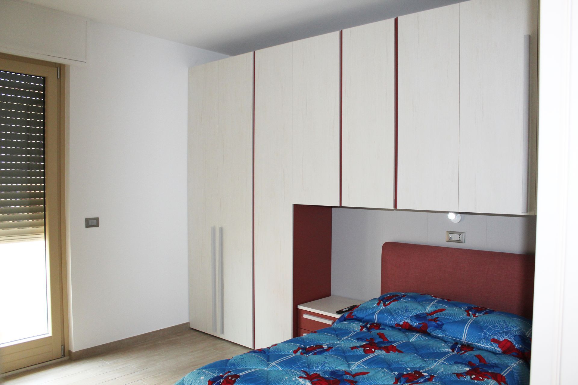 Camera da letto con letto, grande armadio bianco e finestra chiusa con persiane.