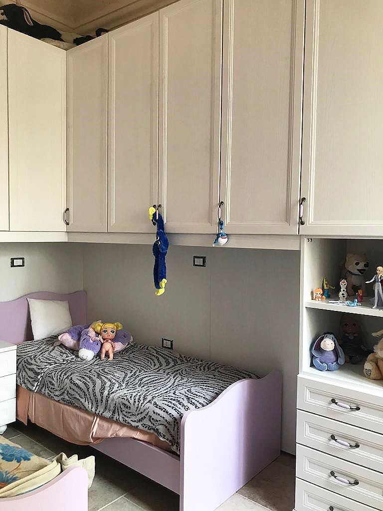 Camera da letto per bambini con letto, armadi bianchi, scaffali per giocattoli e giocattoli sul letto.