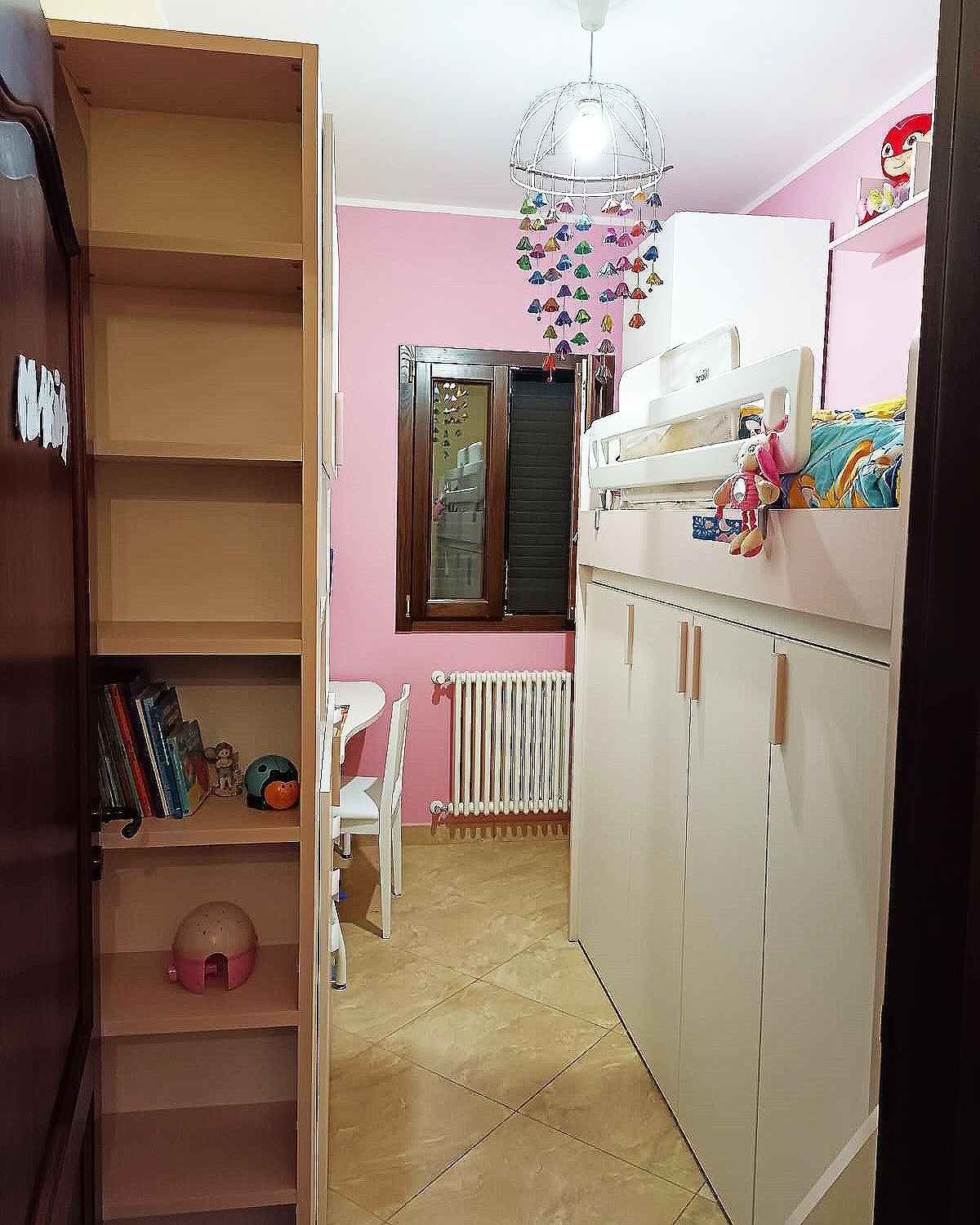 Corridoio stretto con pareti rosa, spazio per riporre gli oggetti e una libreria. Sono visibili una finestra e un tavolino.