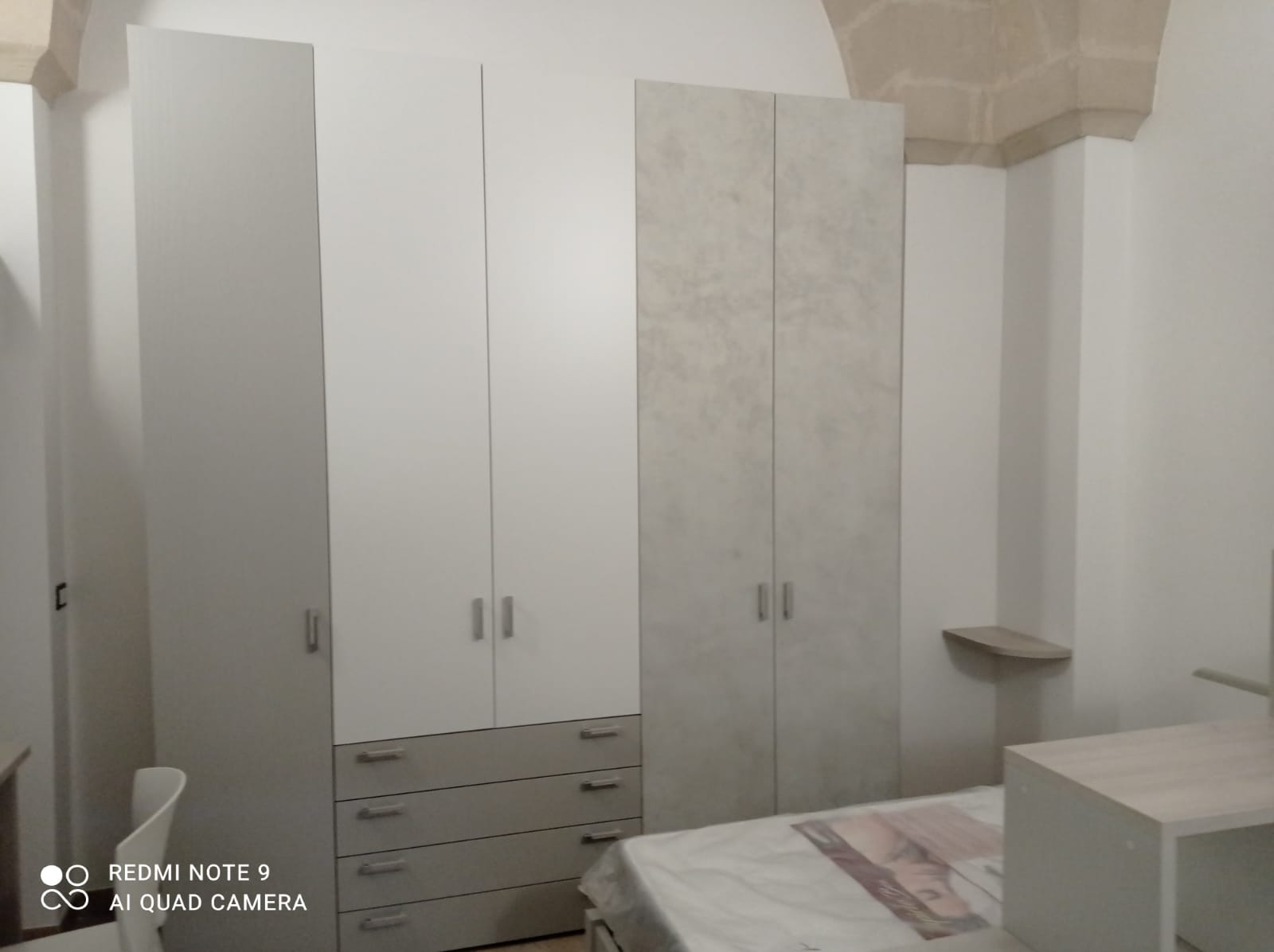 Camera da letto con tre armadi bianchi e grigi, un letto e una scrivania.