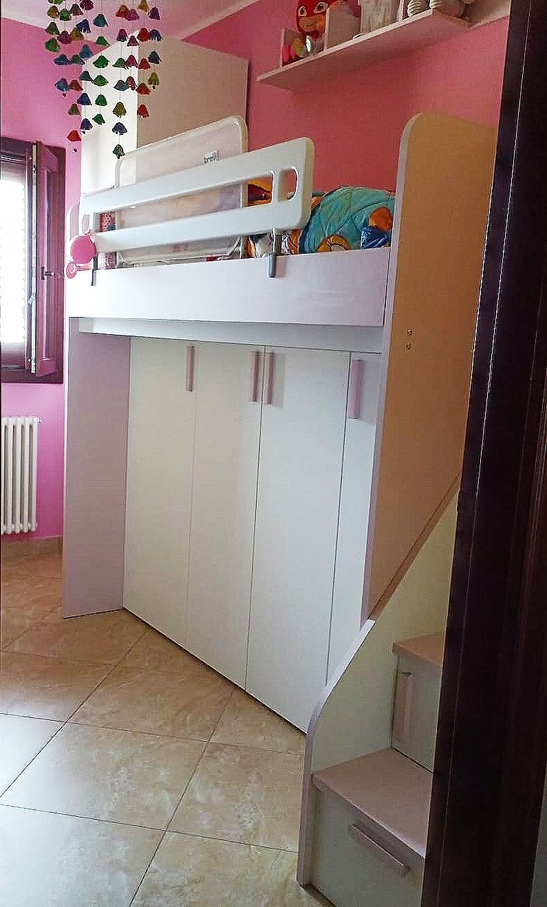Letto a soppalco bianco in una stanza rosa, con scale. Giocattoli e decorazioni a vista.