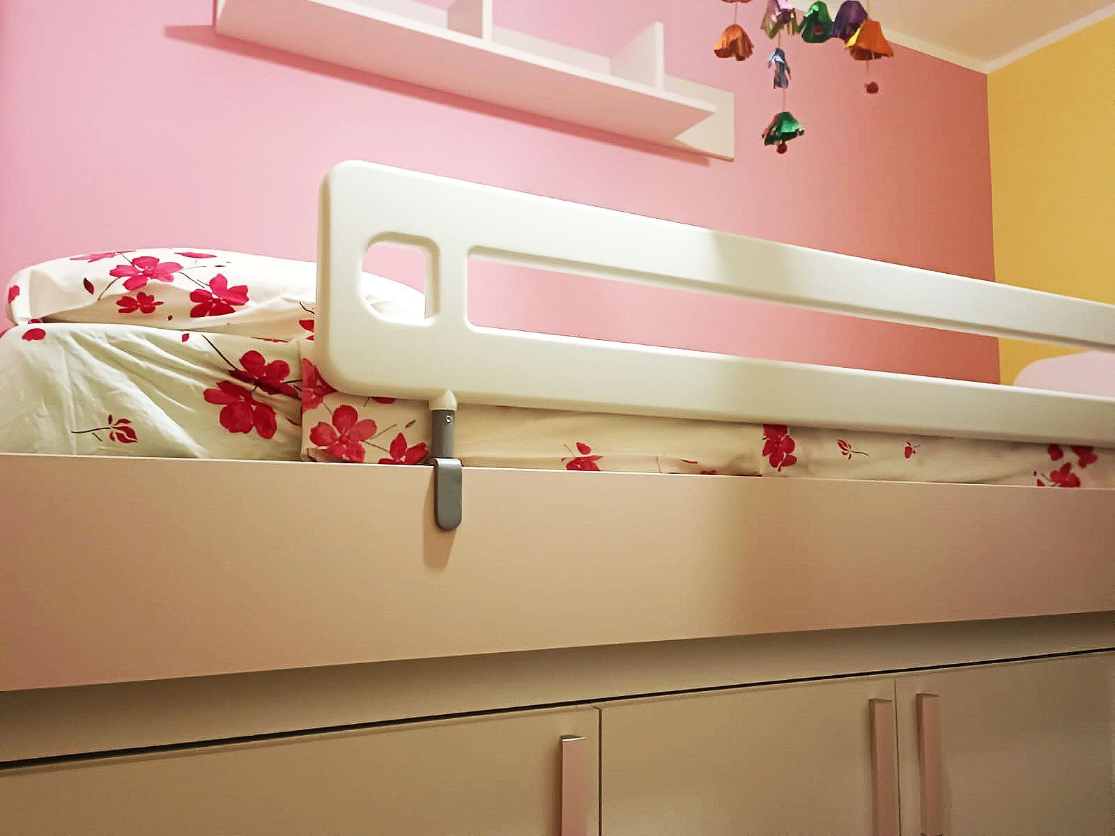 Sponda del letto bianca su un letto bianco con biancheria da letto floreale, in una stanza con pareti rosa e gialle.