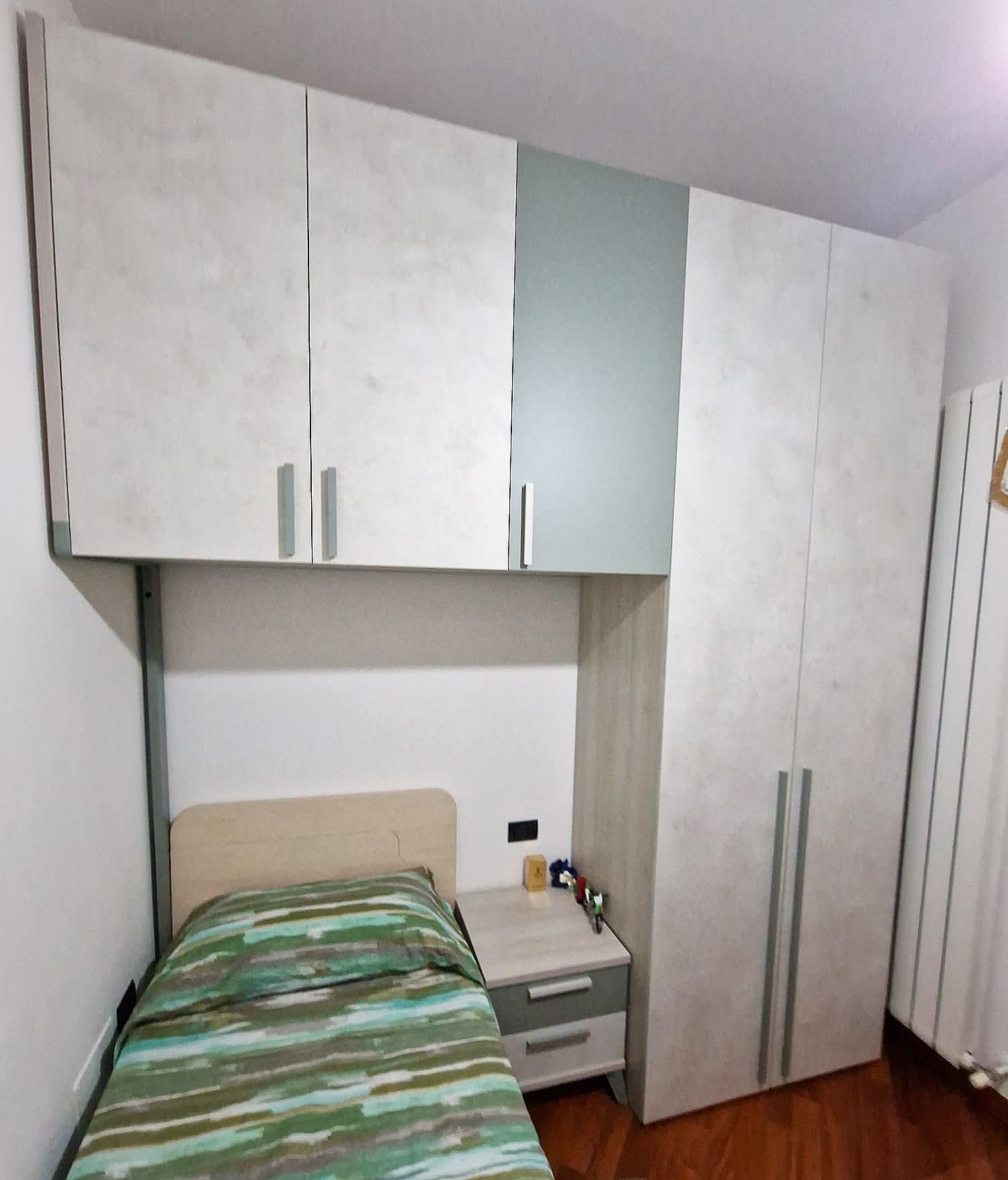 Camera da letto con armadio, letto e comodino bianchi e grigi. Copriletto verde e bianco.