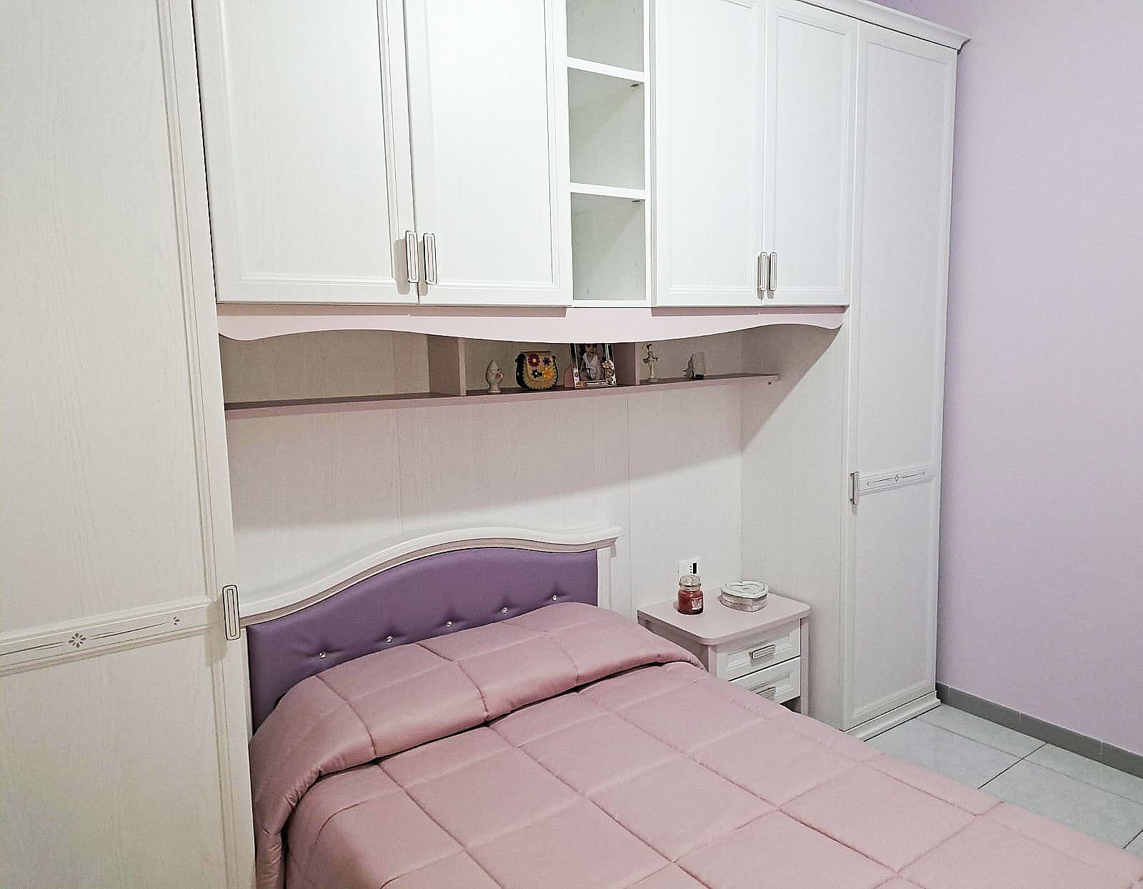 Camera da letto con letto, comodino e armadi bianchi. Pareti viola.