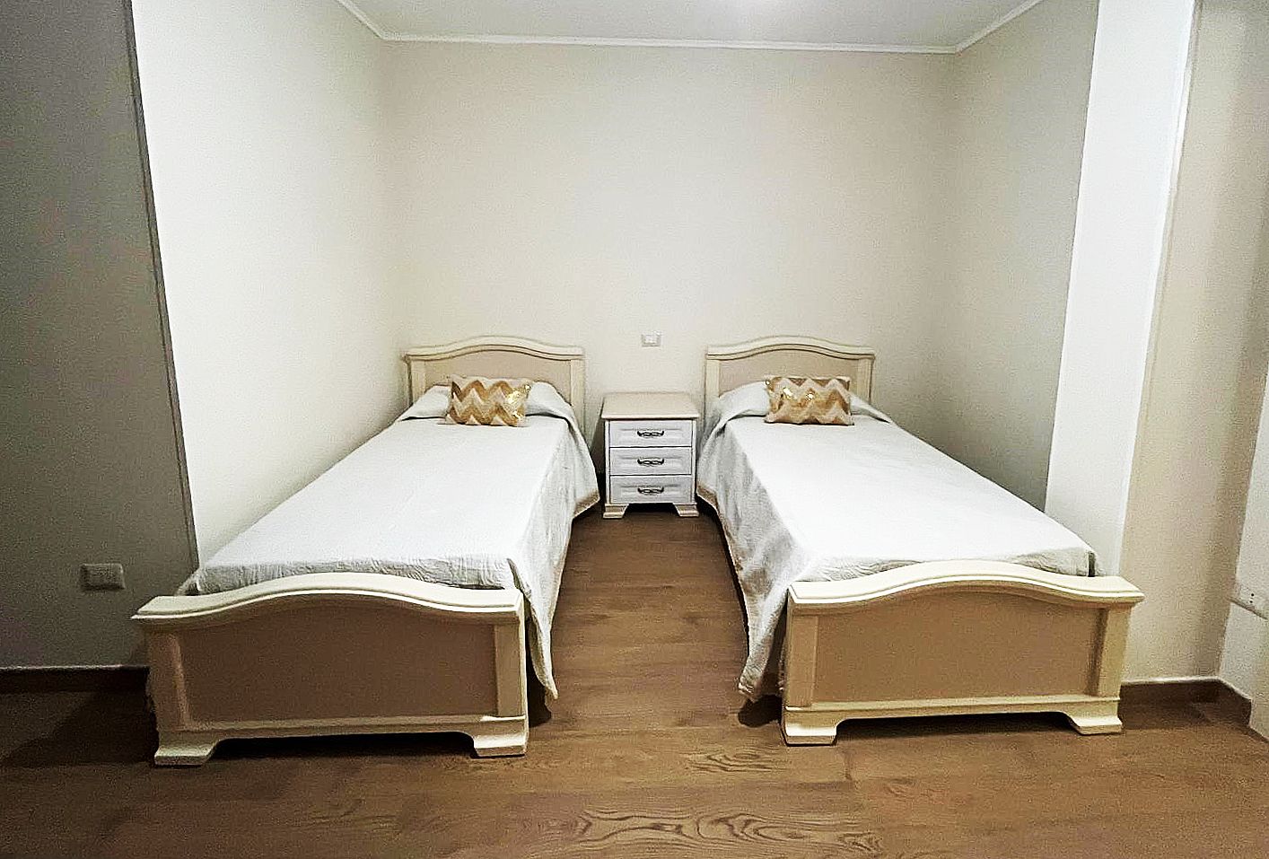 Due letti singoli con lenzuola bianche e un comodino in una camera da letto.