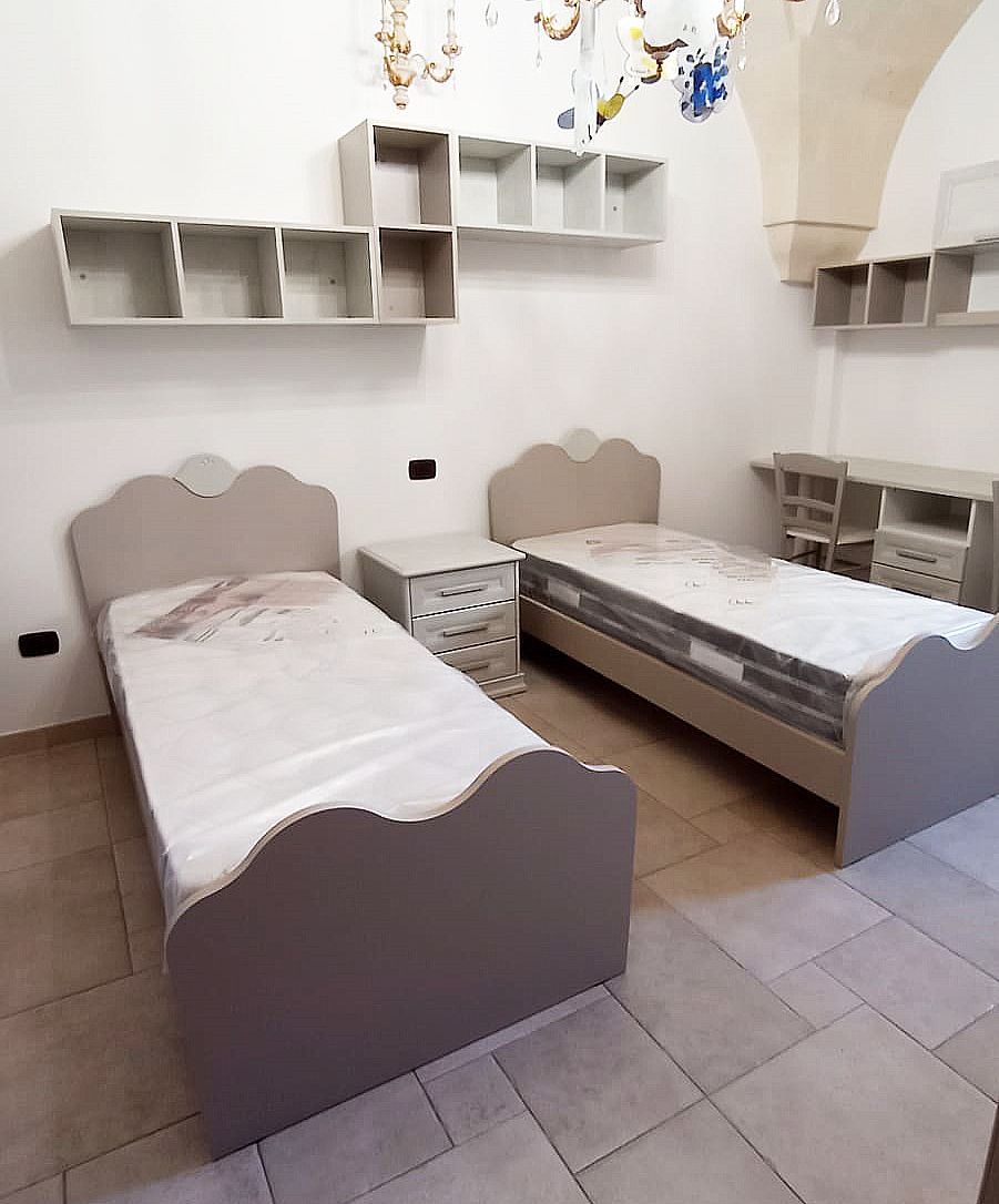 Due letti singoli beige in una stanza con mensole coordinate. Un comodino si trova tra i letti.