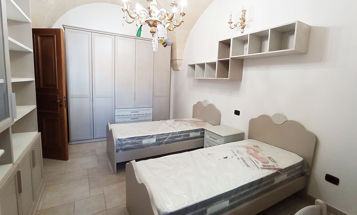 Camera da letto con due letti singoli, armadio, scaffali e lampadario.