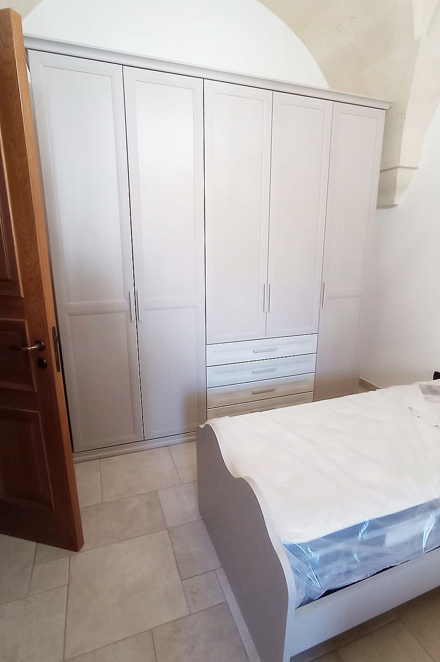 Armadio bianco e letto in una stanza con una porta di legno parzialmente aperta.