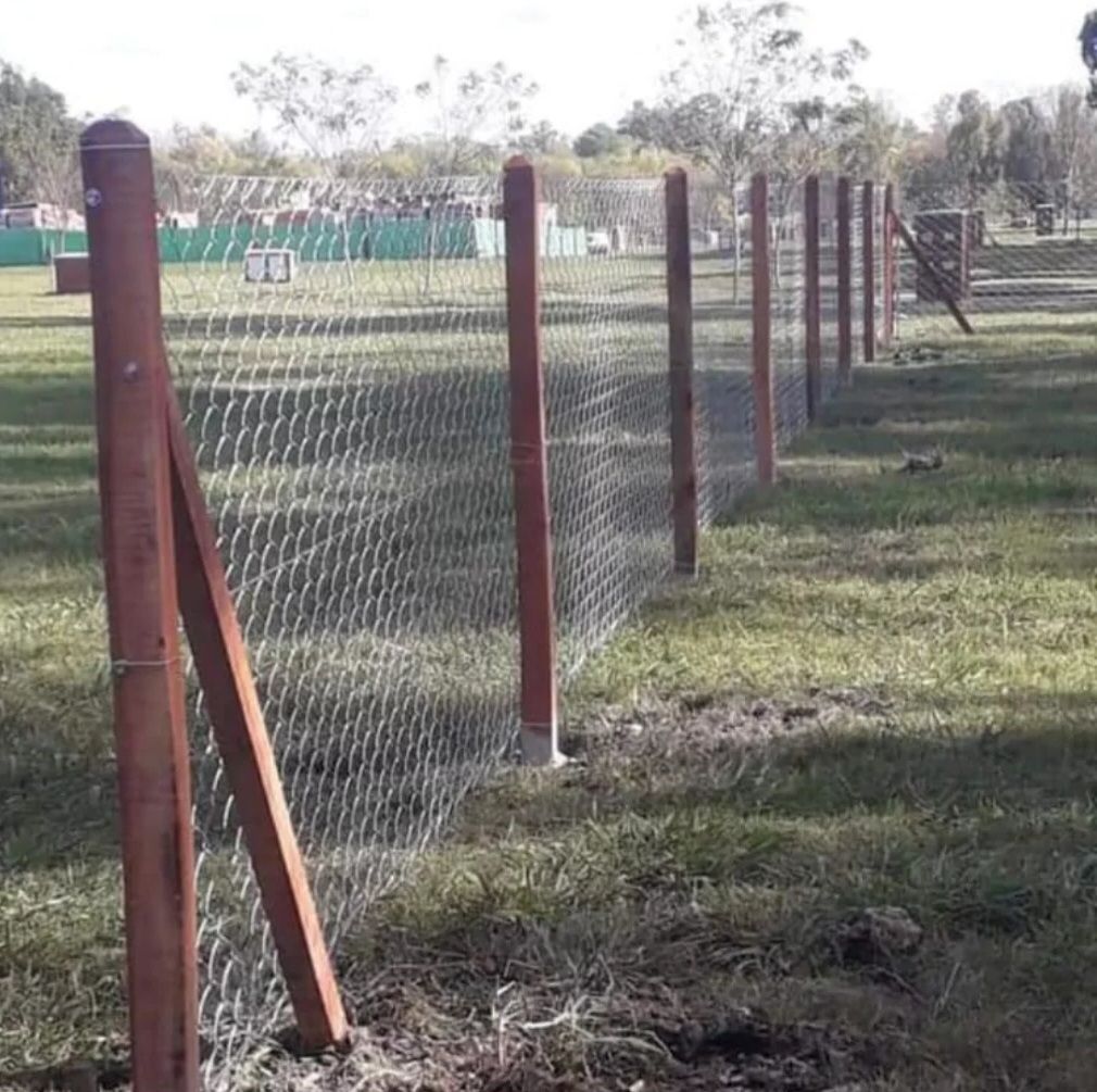 Valla de malla metálica con postes de madera que atraviesa un campo de hierba