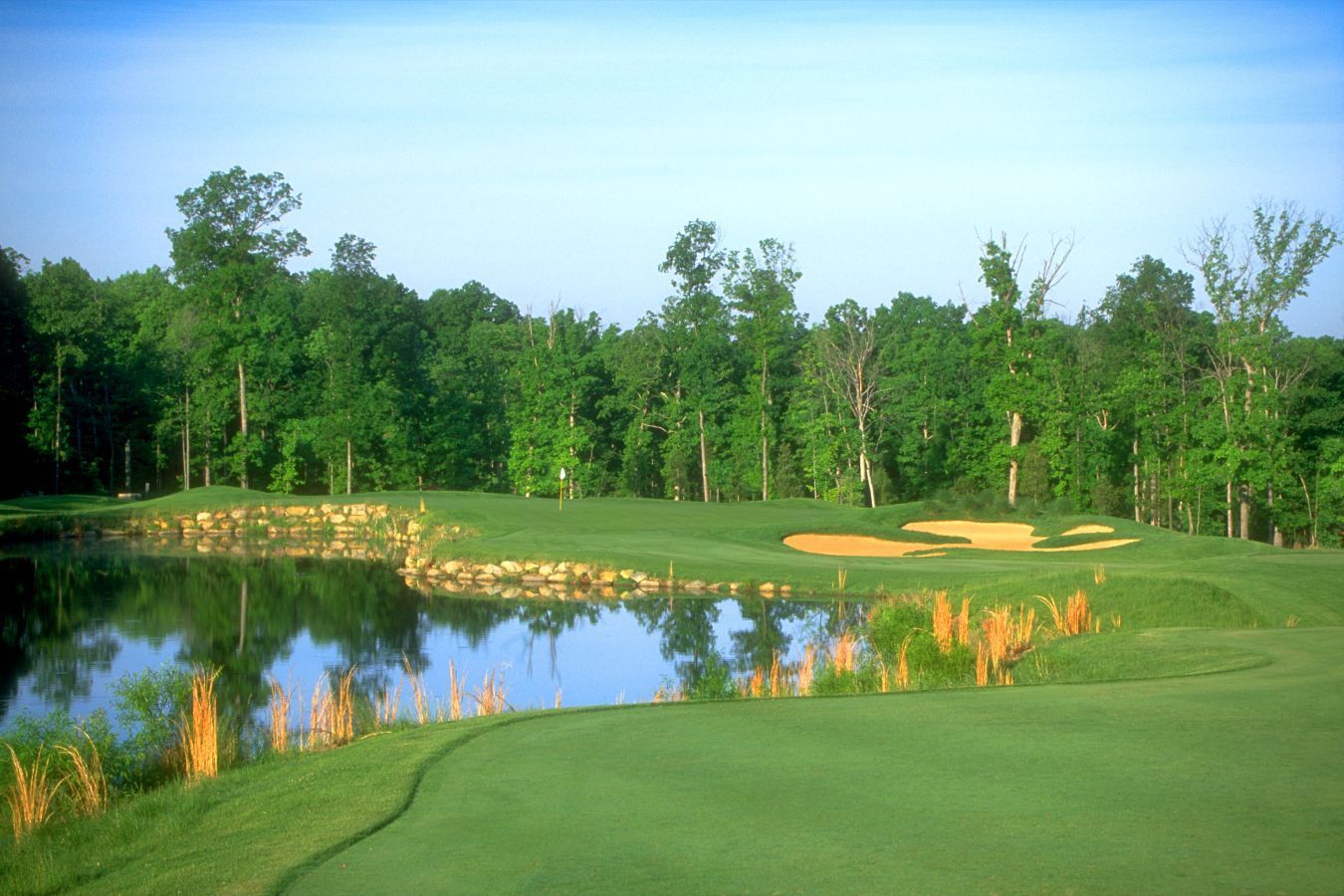 Golf course hole with water, green grass, trees, and blue sky.