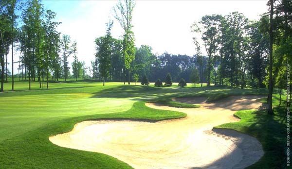 Green golf course with sand traps and trees, sunny day.