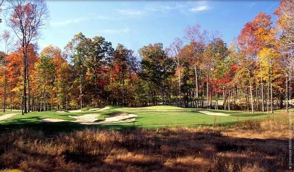 Golf course in autumn. Green fairways and colorful trees under a blue sky.