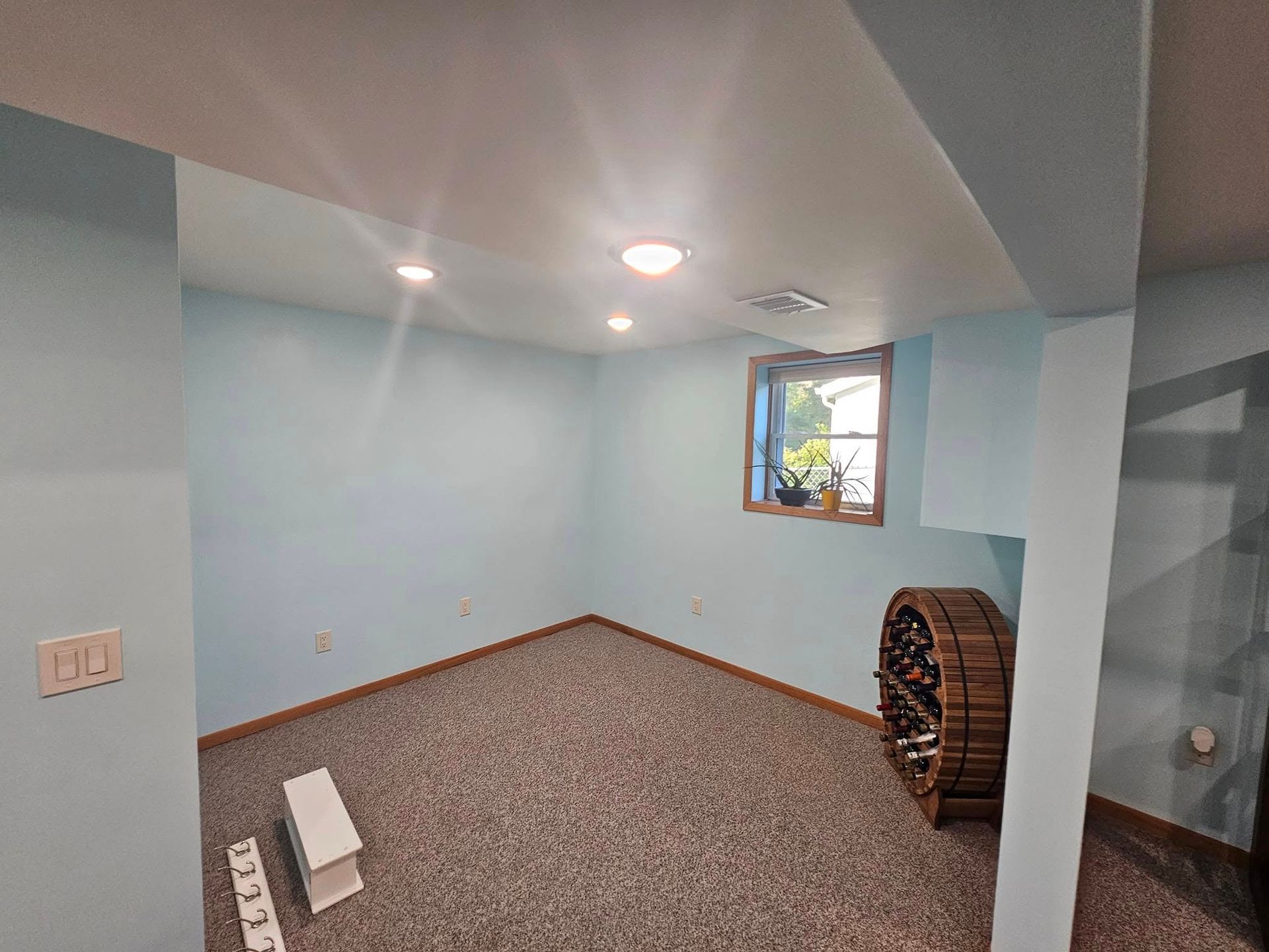 Empty room with blue walls, carpet, window, wine rack, and ceiling lights.