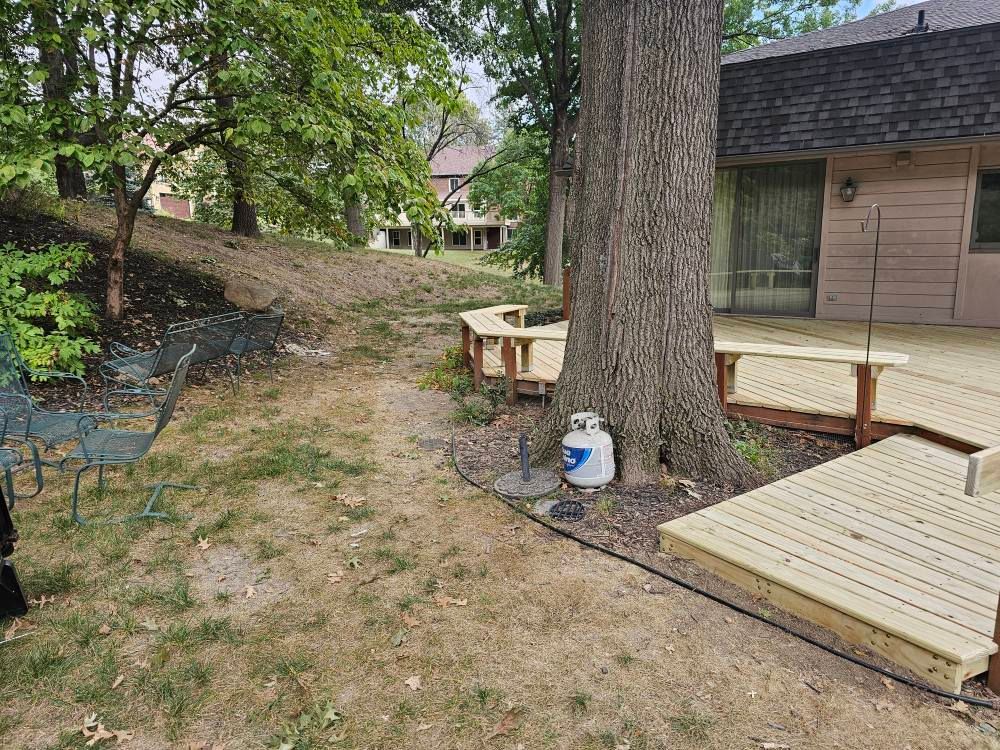 Backyard with wooden decks around a tree, propane tank visible.
