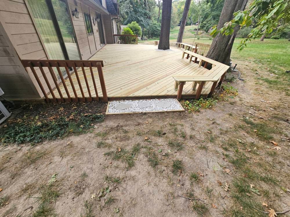 Wooden deck with railing, steps, and built-in benches, adjacent to a grassy yard and trees.