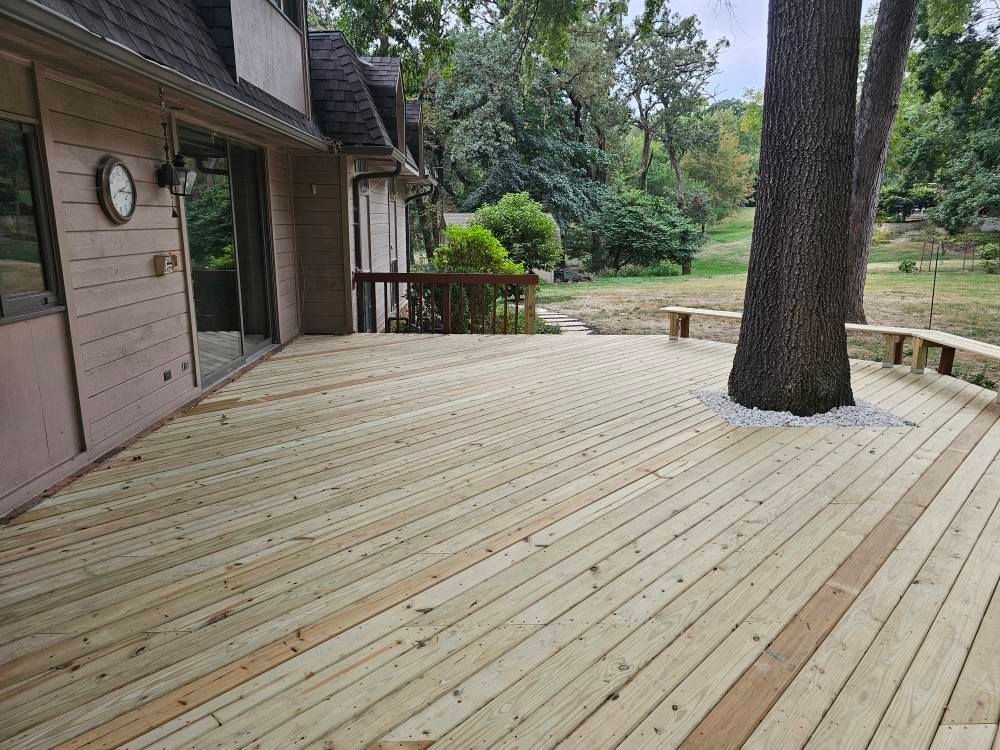 Wooden deck wraps around a tree with a view of a yard and house.