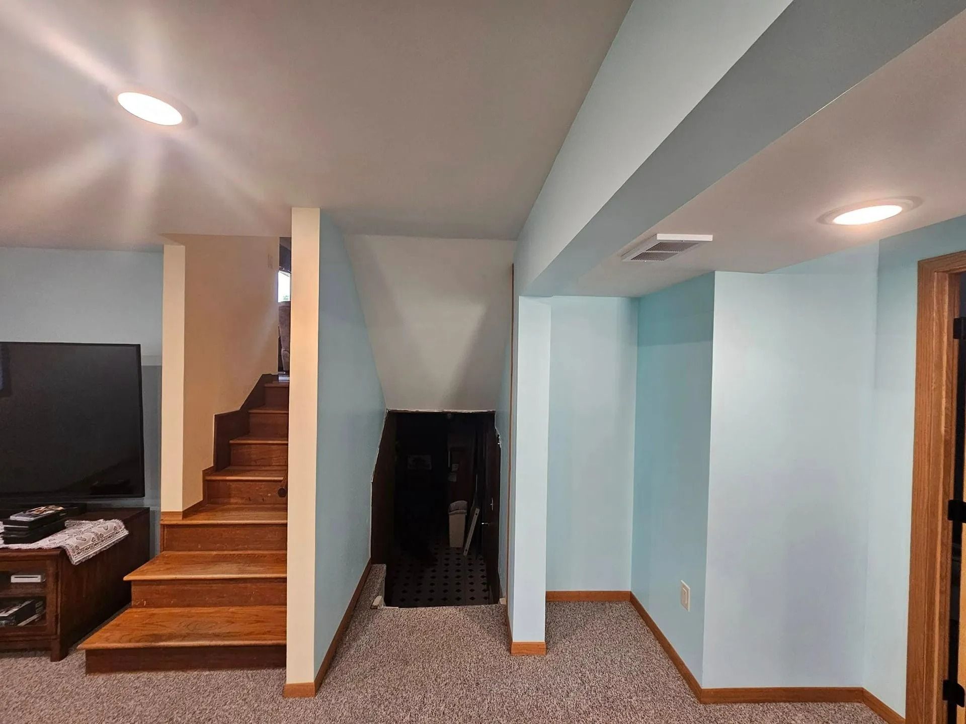 Basement interior with stairs, blue walls, brown wooden door. Brown carpet floor.