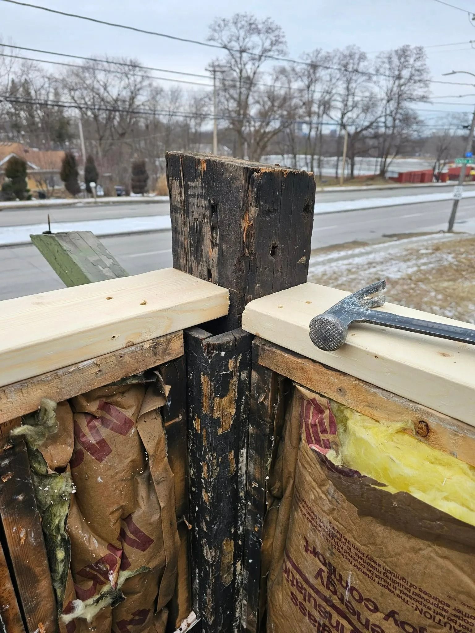 Corner of a building under construction.  Black post surrounded by new wooden beams. Hammer on the wood.