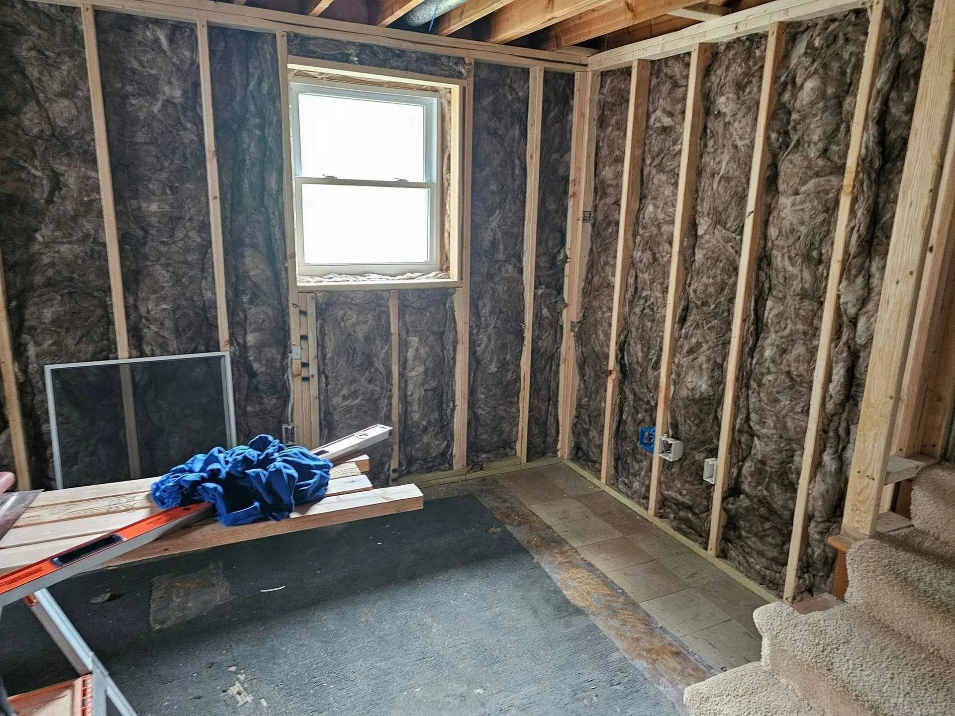 Interior view of a room under construction, insulated walls, window, bare studs, and unfinished floor.