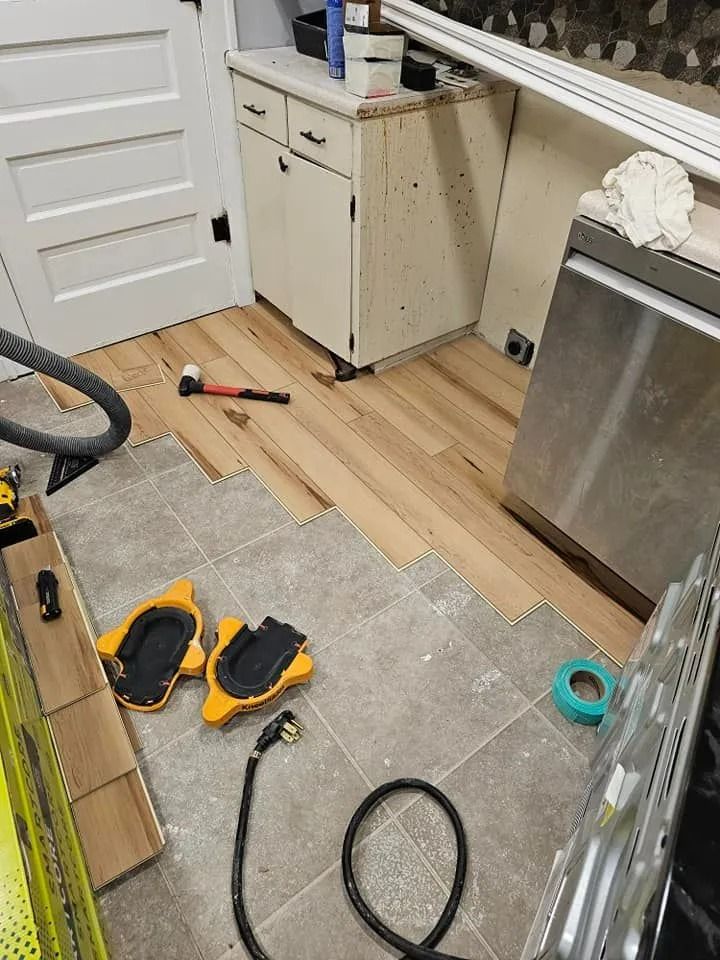 Flooring renovation: New hardwood being installed over tile floor. Tools and materials are scattered in a kitchen.