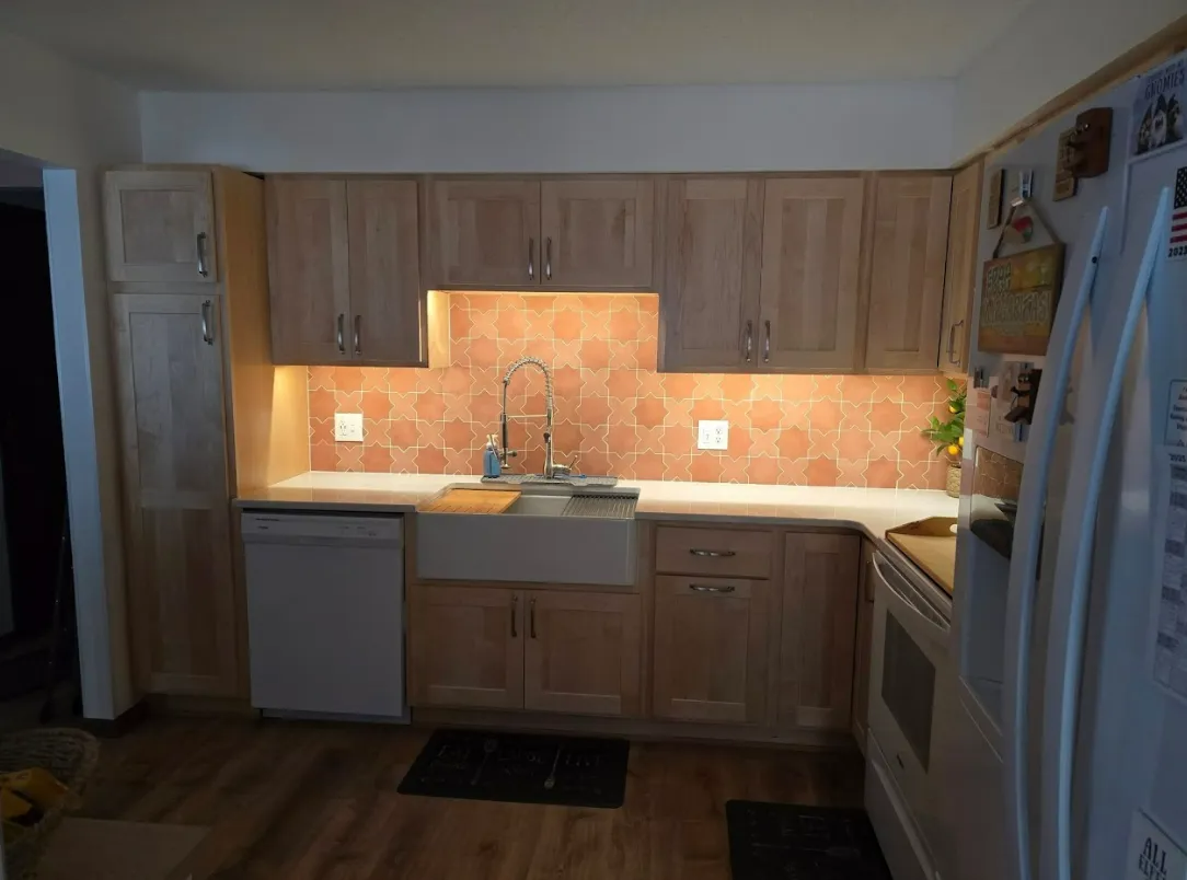 Kitchen with light wood cabinets, white sink, red-brown backsplash, and white appliances.