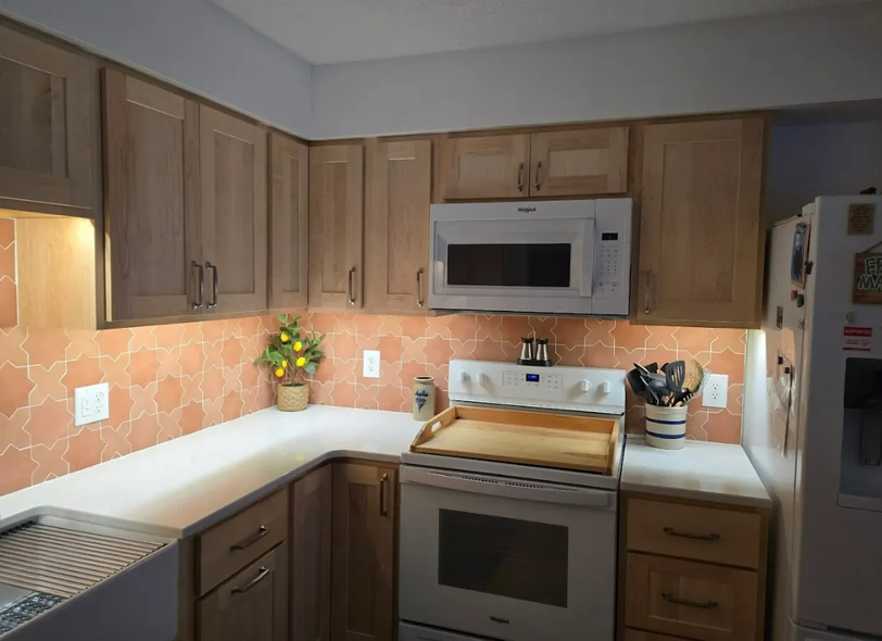 Kitchen with light wood cabinets, white countertops, orange tile backsplash, and appliances.