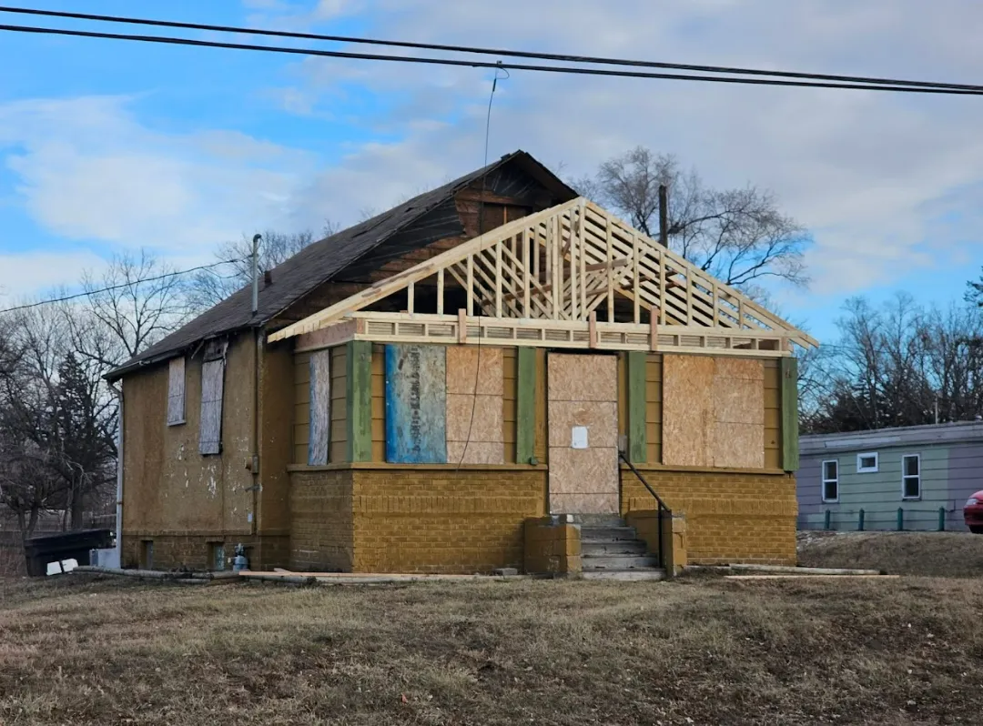 Dilapidated building with new roof framing; boarded-up windows, outdoors.