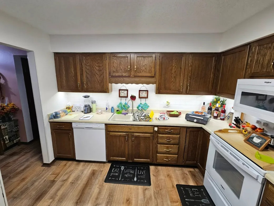 Kitchen with brown cabinets, white appliances, and light-colored countertops. Wood-look flooring.