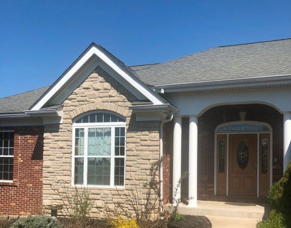 Suburban brick and stone house facade with arched entryway, white columns, and double front doors