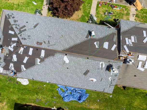 Aerial view of a roof covered with scattered debris and tarps after storm damage