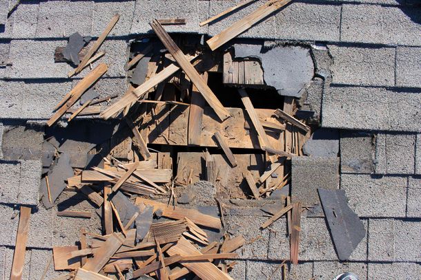 Damaged roof shingles with a large hole exposing broken wood beneath