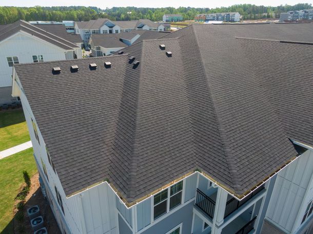 Aerial view of a brown shingle roof on a townhouse with dormers and nearby homes in a suburban neighborhood