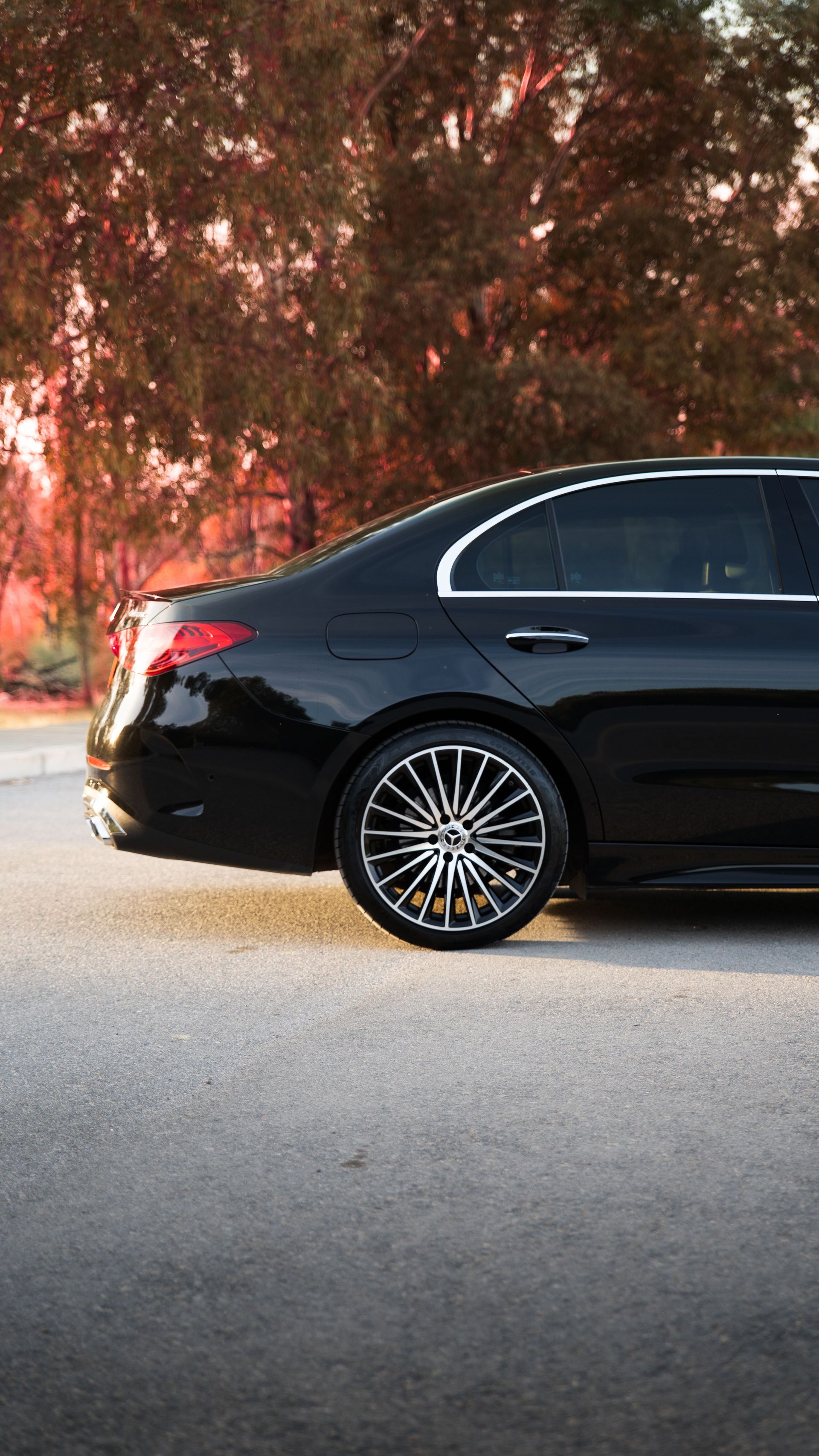 Black sedan parked on a street, side view, with trees and warm sunset light in the background