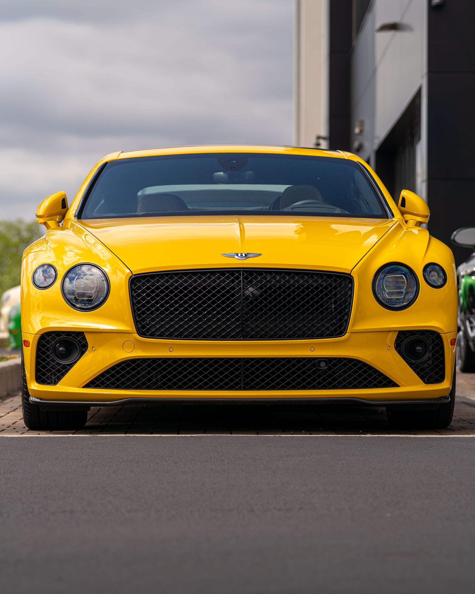 Yellow Bentley sports car parked outdoors near a building, front view