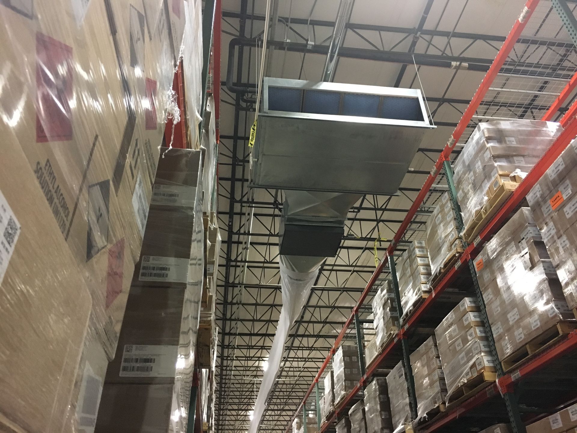 Warehouse aisle with stacked boxes and overhead ductwork between tall pallet racks