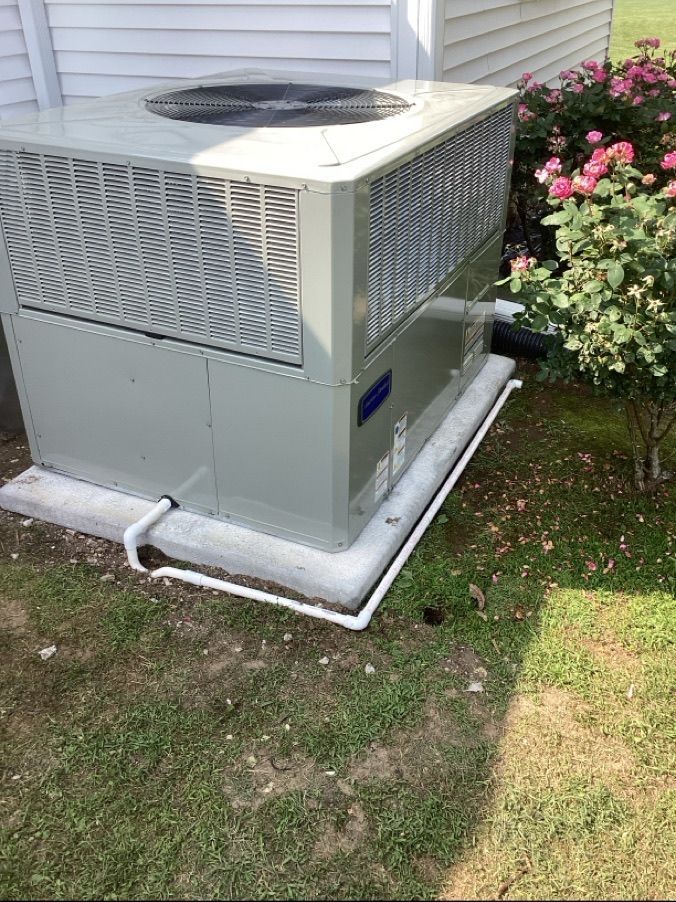 Outdoor air conditioner unit beside a house, next to flower bushes and a grassy yard.