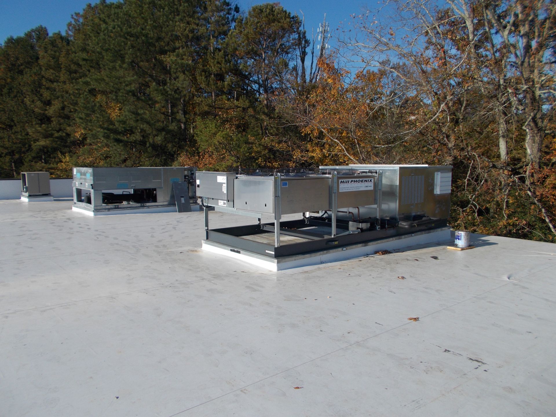 Rooftop HVAC units on a flat white roof with trees in the background