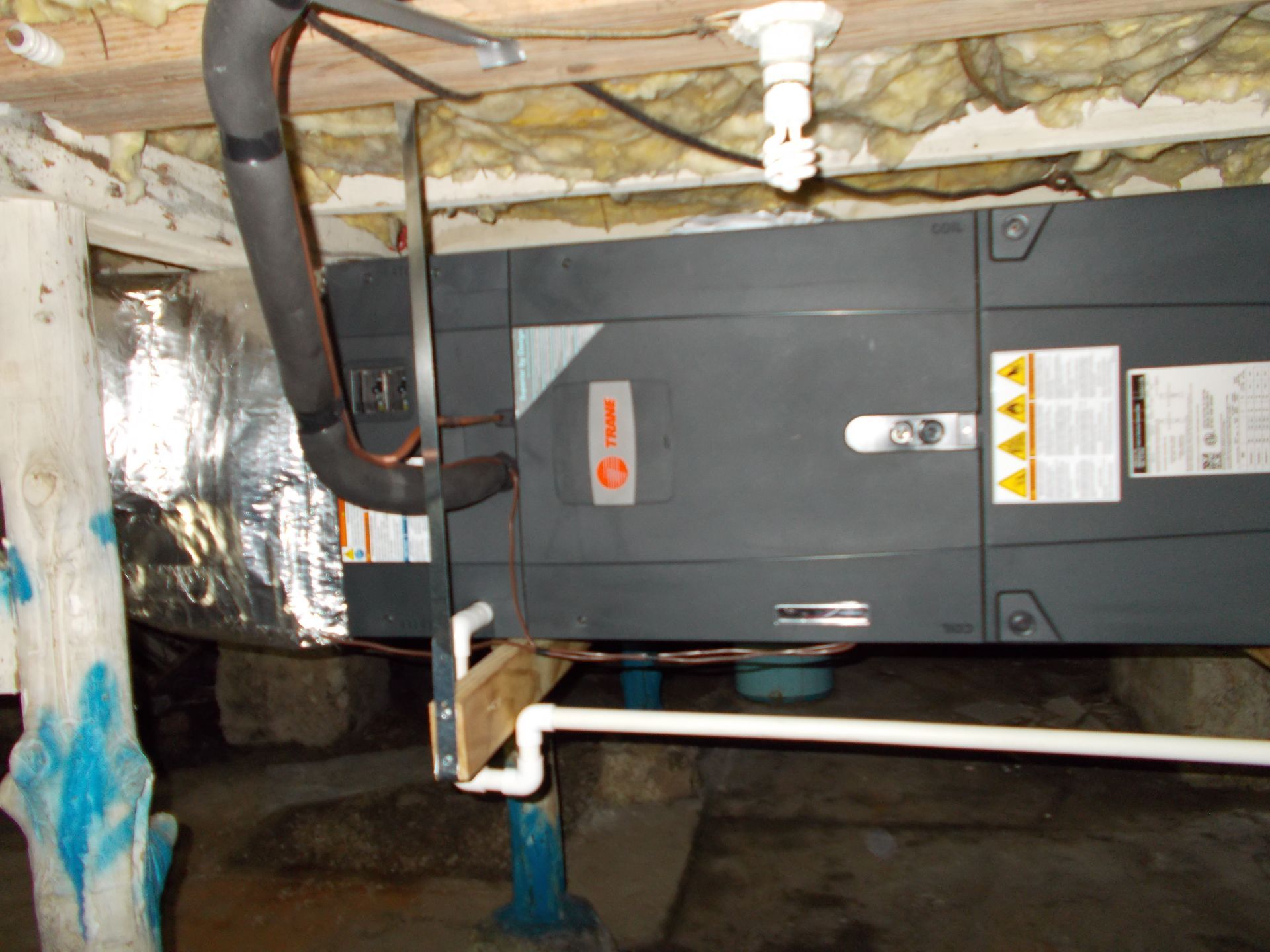 Gray HVAC unit in a basement crawl space with exposed pipes and insulation.