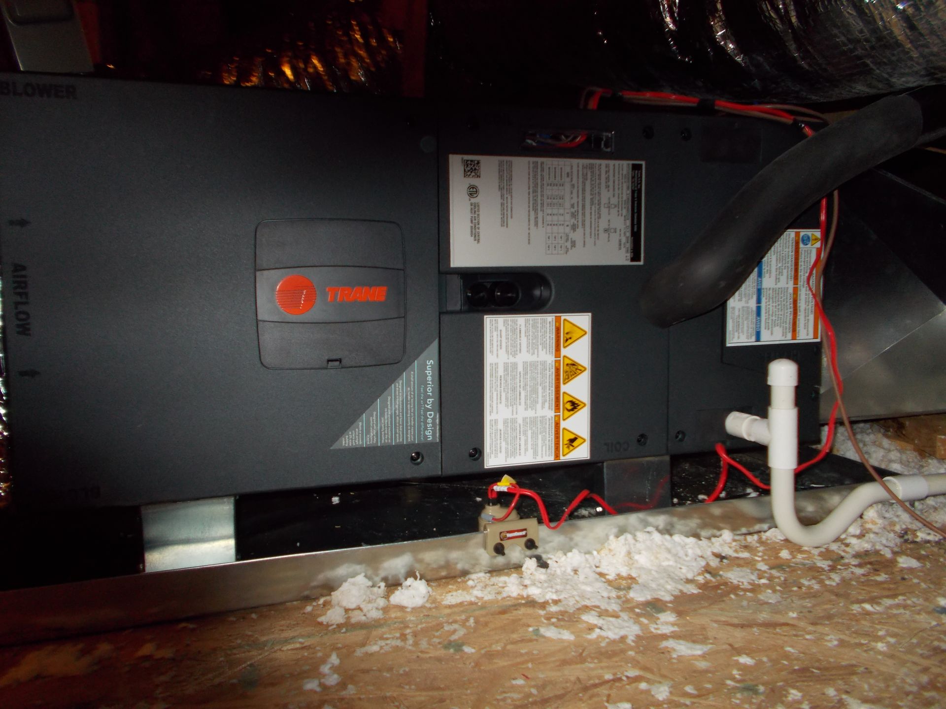Gray furnace unit in a crawlspace, surrounded by exposed pipes and debris on the floor.