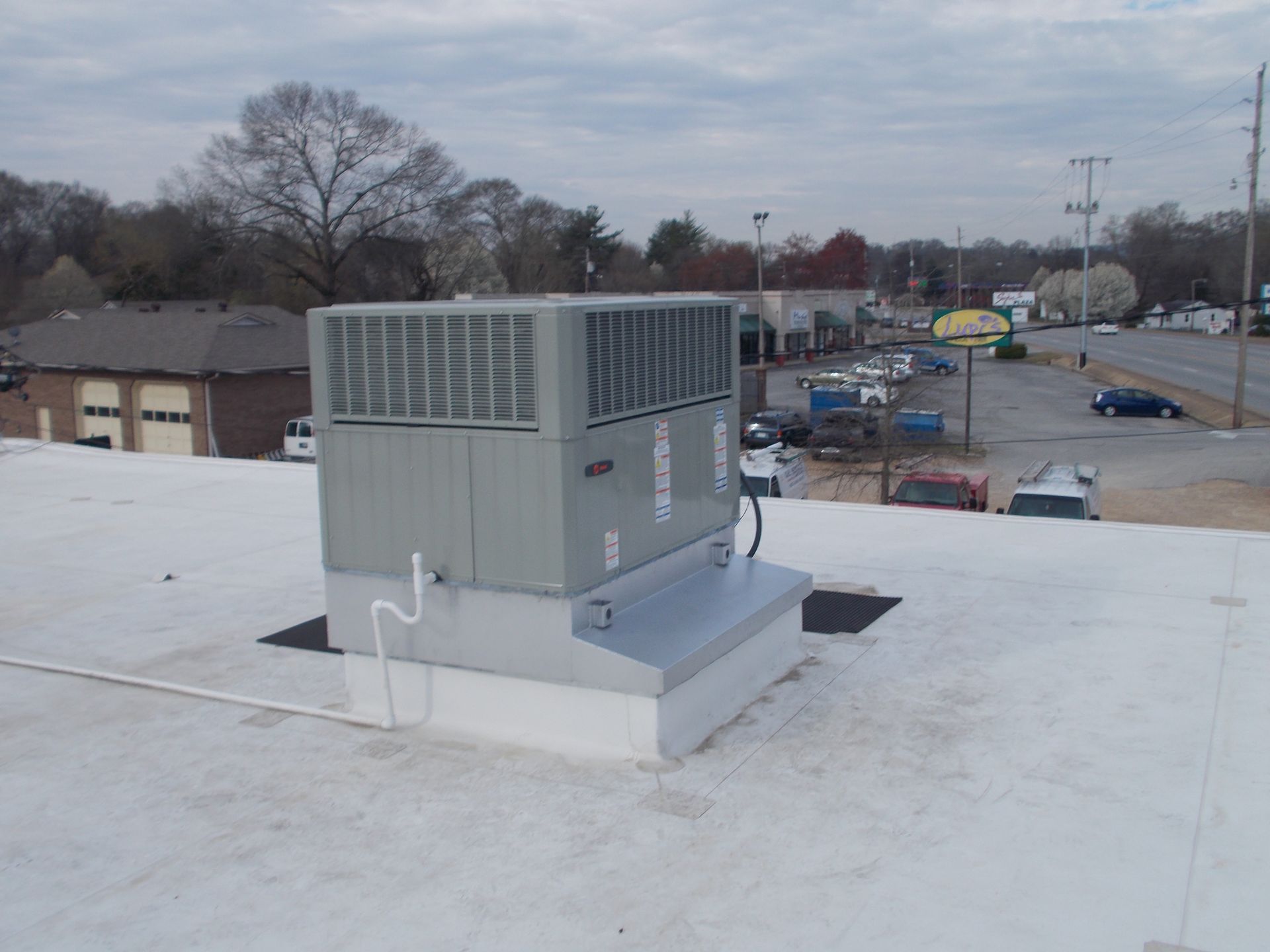 Rooftop HVAC unit on a flat white roof overlooking a parking lot and street.