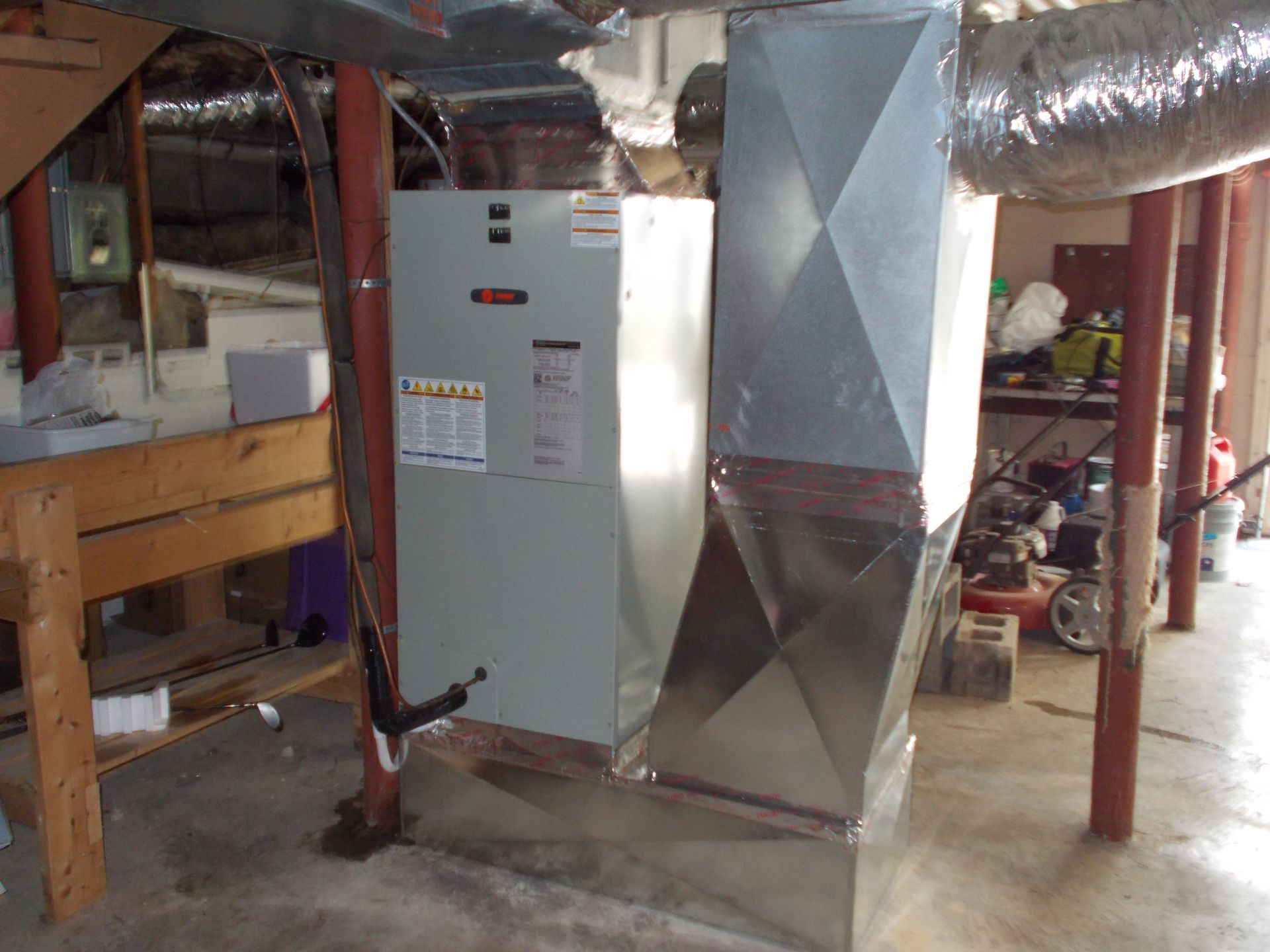 Two workers install a large HVAC unit on a flatbed truck using lifting straps.