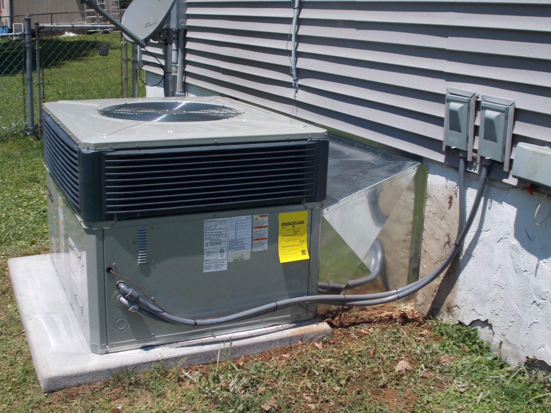 Outdoor HVAC unit beside a house, with black top vents and gray body on a concrete pad.