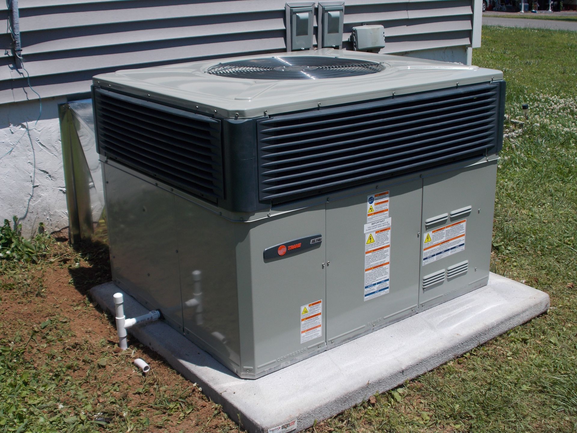 Outdoor HVAC unit on a concrete pad beside a house, with gray panels and black vents.
