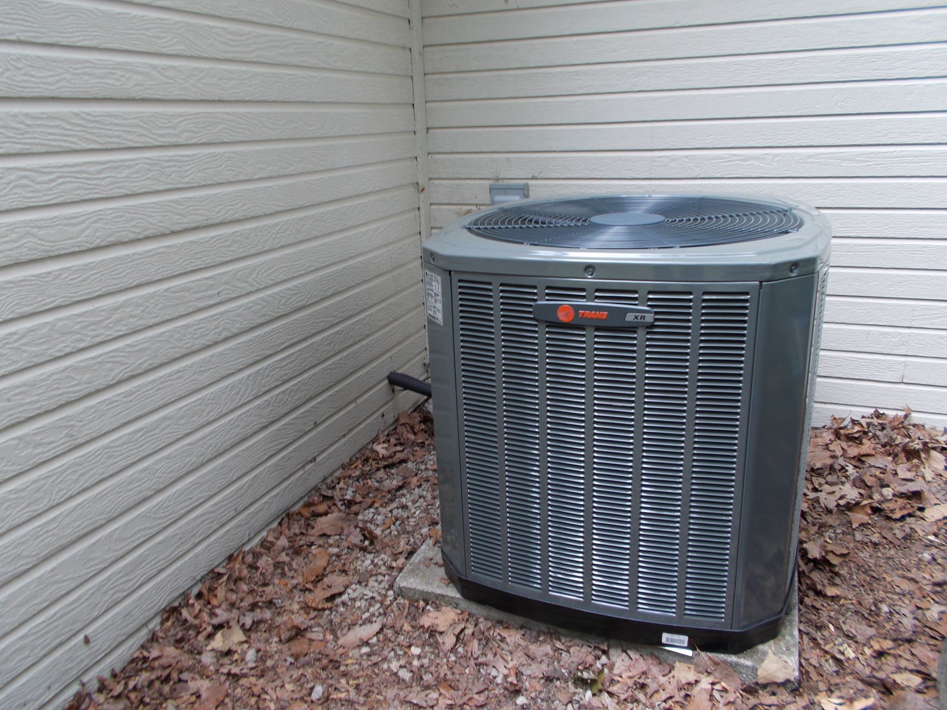 Outdoor central air conditioner unit beside a house wall and utility meters, with grass and a satellite dish nearby