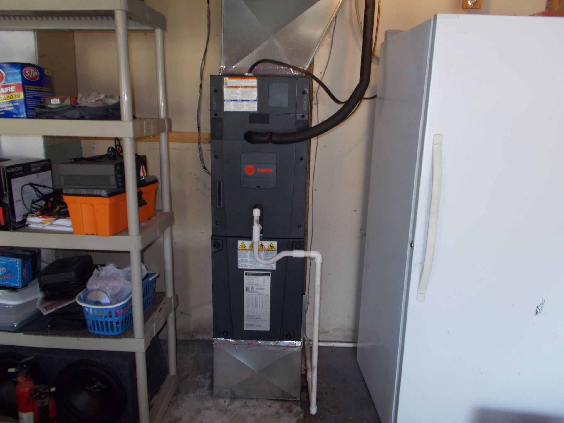Garage utility area with a black furnace beside a white refrigerator and metal shelving unit