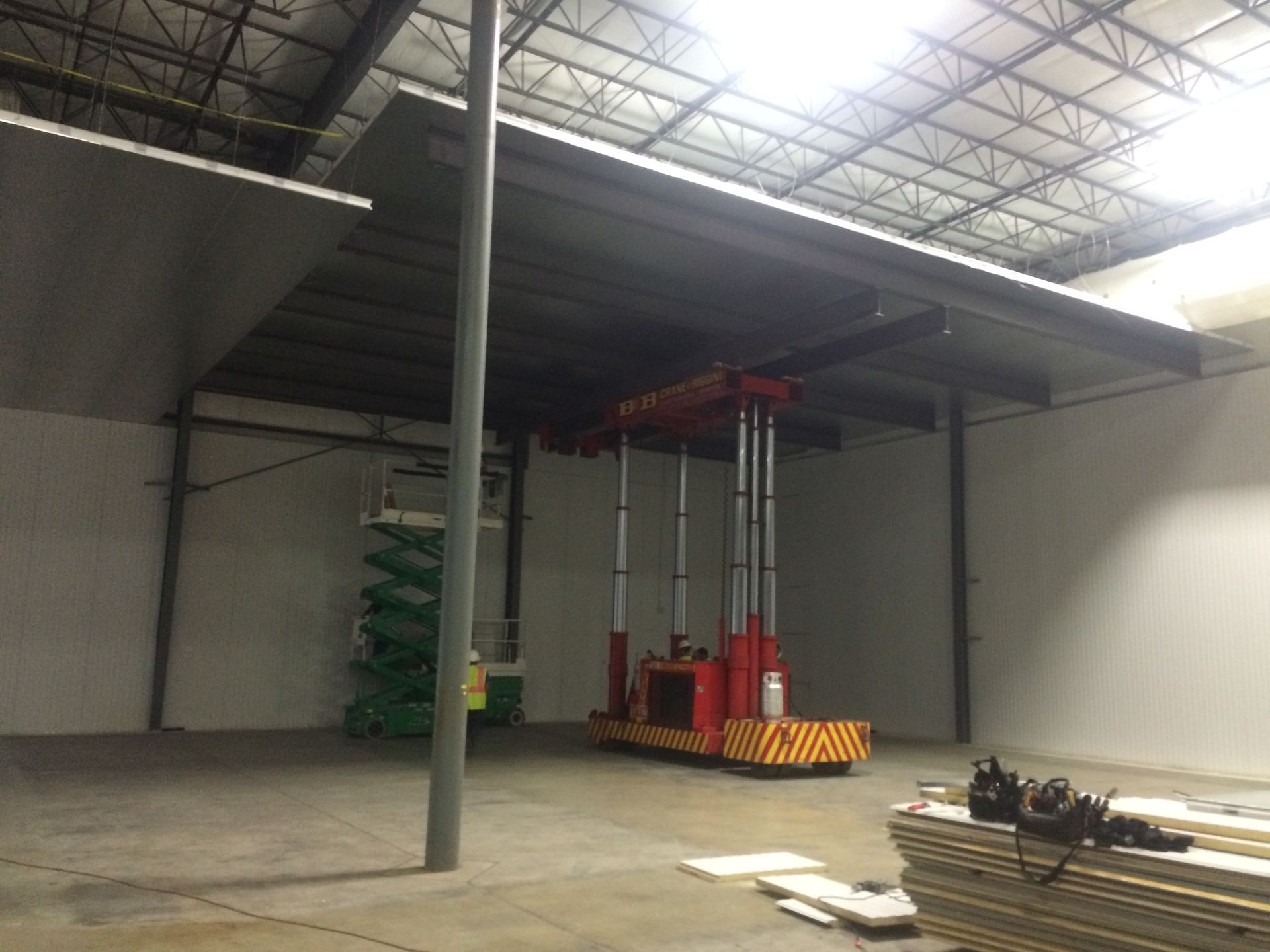 Empty warehouse interior with a red lift near stacked pallets and a high metal ceiling
