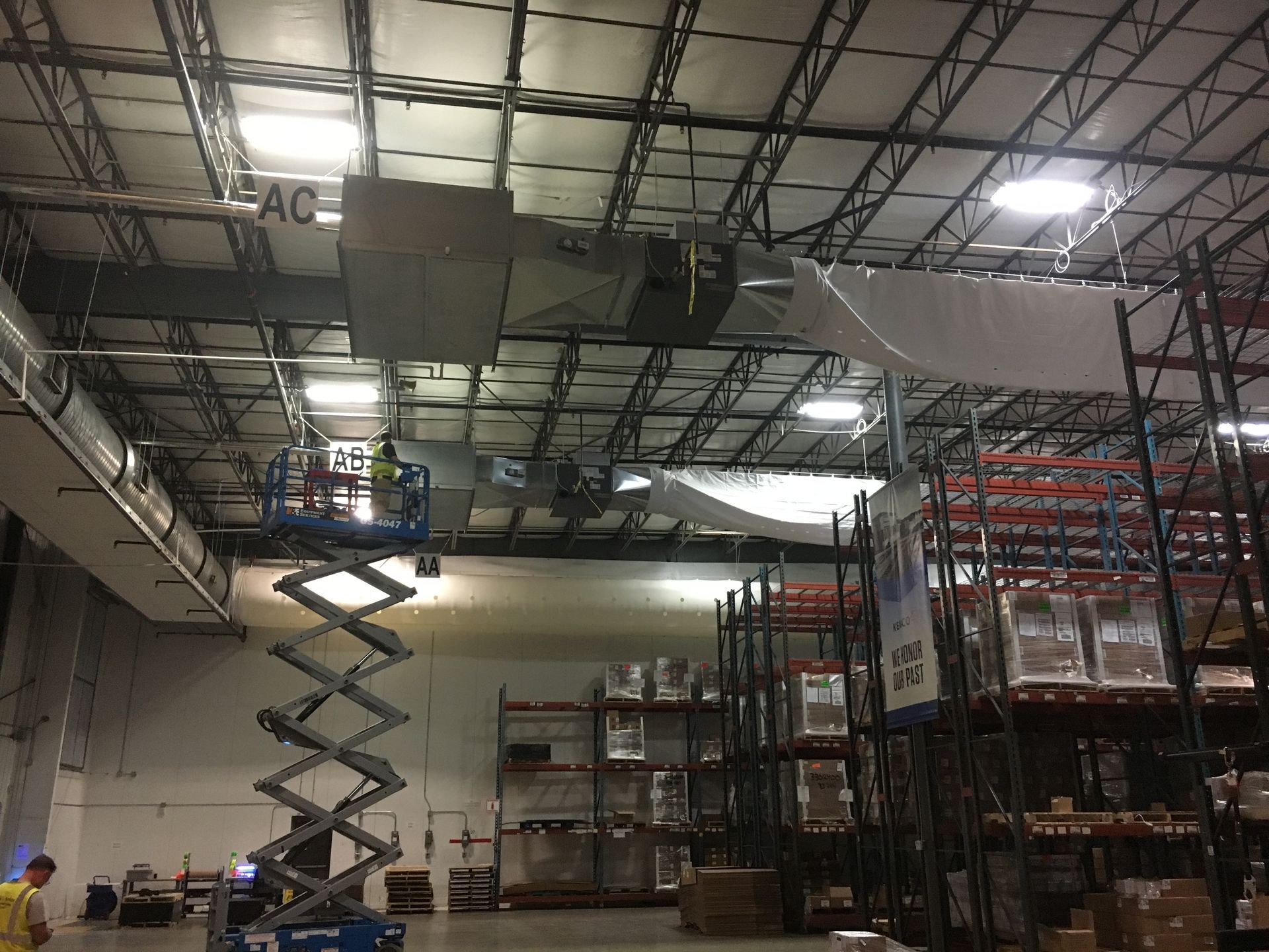 Warehouse interior with a scissor lift raised toward the ceiling and storage racks on the right.